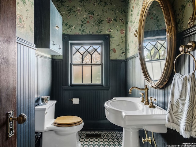 half bathroom featuring plenty of natural light, toilet, wainscoting, and wallpapered walls