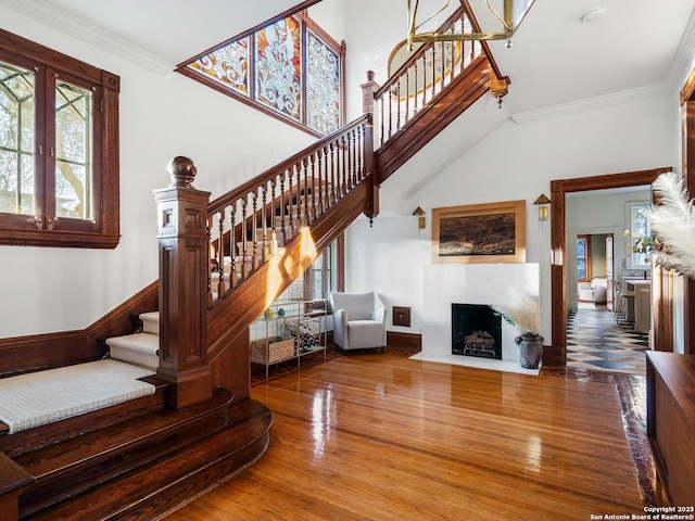 stairway featuring a fireplace with flush hearth, a high ceiling, wood finished floors, and crown molding