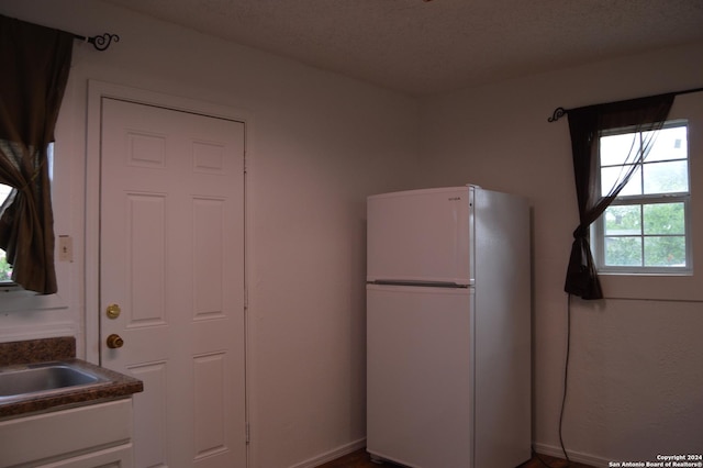 kitchen featuring a textured ceiling, dark countertops, freestanding refrigerator, and white cabinets