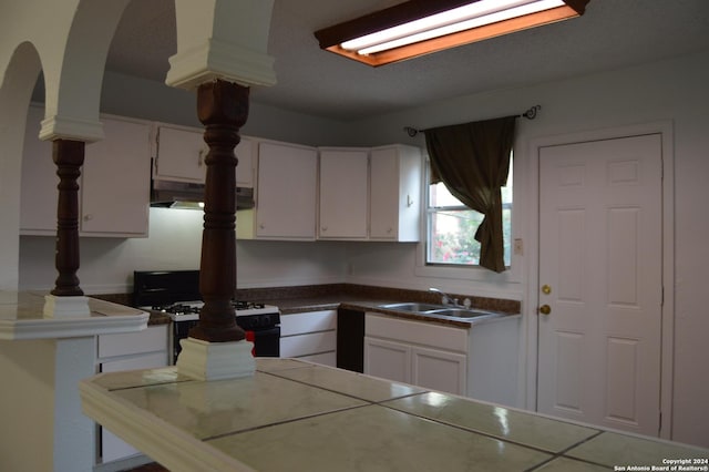 kitchen with arched walkways, white cabinets, a sink, under cabinet range hood, and white gas range oven