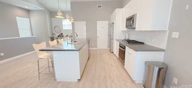 kitchen featuring visible vents, white cabinets, a kitchen breakfast bar, stainless steel appliances, and a sink