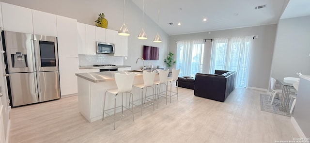 kitchen with light wood finished floors, tasteful backsplash, appliances with stainless steel finishes, and a breakfast bar area