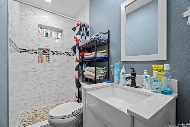 bathroom with vanity, toilet, a textured wall, and a tile shower