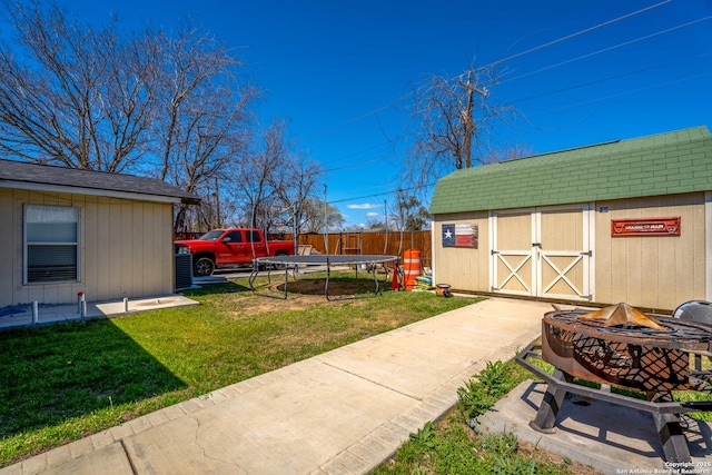 view of yard with a trampoline, fence, an outdoor fire pit, a storage shed, and an outdoor structure