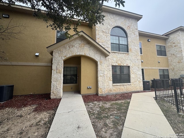 view of front facade featuring stucco siding, fence, and central air condition unit