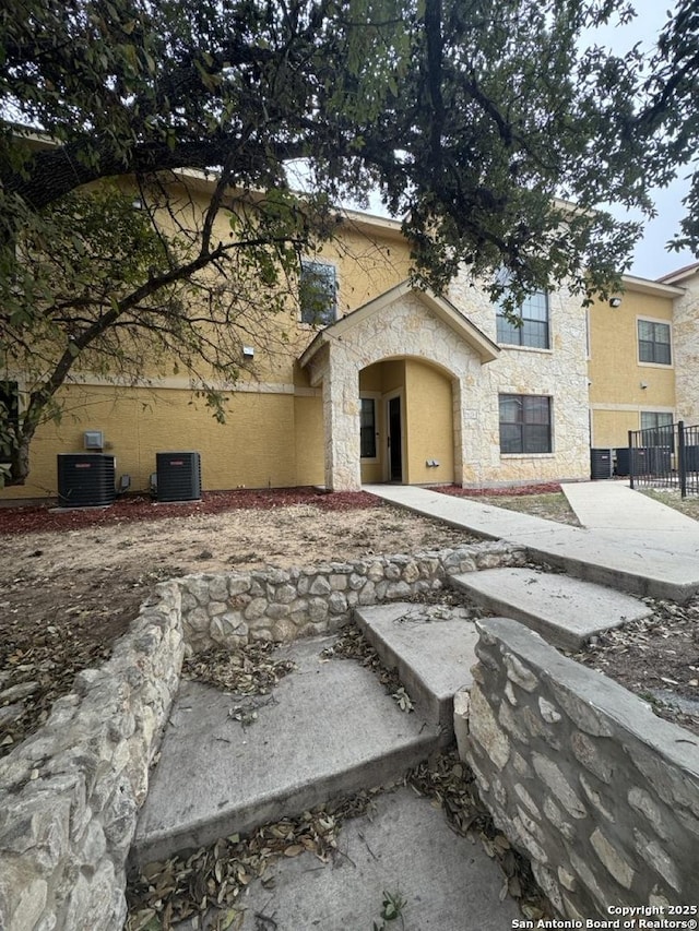 multi unit property featuring stone siding, fence, central AC unit, and stucco siding