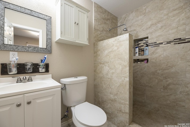 full bath featuring a textured wall, vanity, a tile shower, and toilet