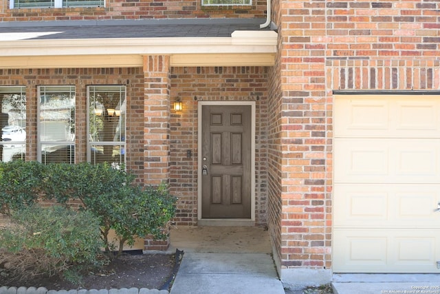 doorway to property featuring an attached garage, roof with shingles, and brick siding