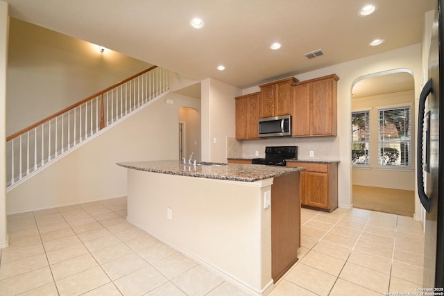 kitchen featuring arched walkways, light tile patterned flooring, a sink, and black appliances