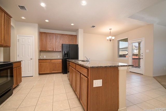 kitchen with light tile patterned floors, visible vents, brown cabinetry, dark stone countertops, and black appliances