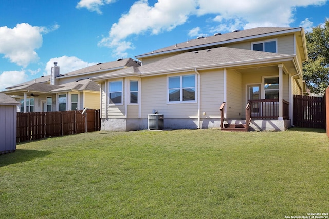 rear view of house with central air condition unit, fence, and a lawn