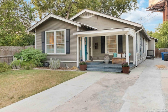 bungalow-style home with covered porch, fence, and a front lawn