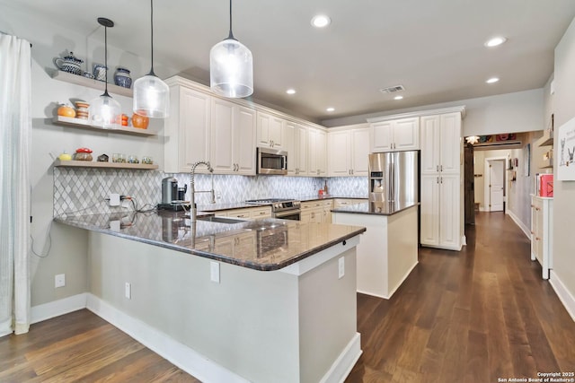 kitchen with stainless steel appliances, decorative backsplash, dark wood-type flooring, a sink, and a peninsula