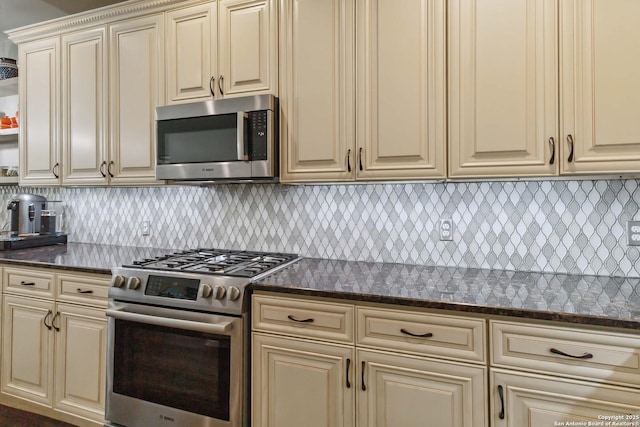 kitchen featuring cream cabinets, dark stone counters, stainless steel appliances, and decorative backsplash