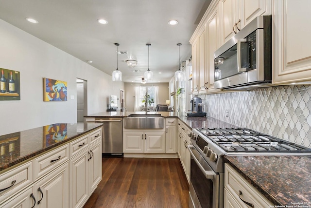 kitchen featuring cream cabinets, stainless steel appliances, a peninsula, dark wood-style flooring, and a sink