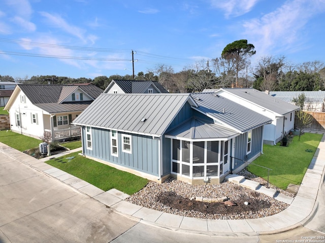 view of front of house featuring board and batten siding, a front yard, a standing seam roof, a sunroom, and metal roof