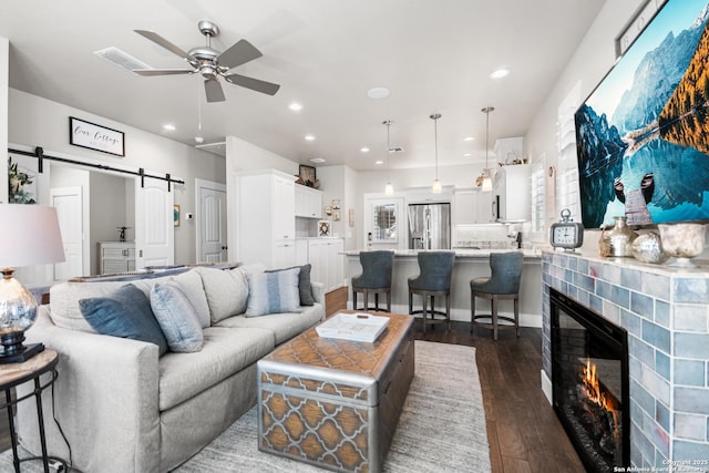 living area featuring a barn door, visible vents, dark wood-style floors, ceiling fan, and a fireplace