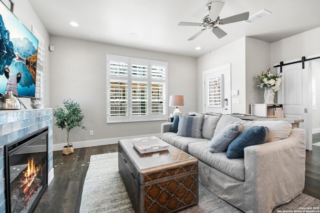 living room featuring a barn door, a fireplace, wood finished floors, visible vents, and a ceiling fan