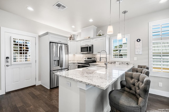 kitchen featuring visible vents, dark wood-style floors, a peninsula, stainless steel appliances, and a sink