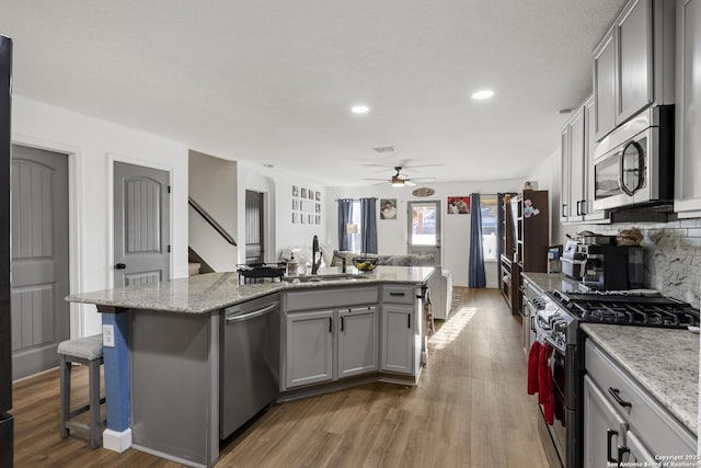 kitchen featuring stainless steel appliances, a sink, a center island with sink, and gray cabinetry