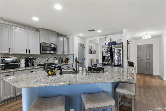 kitchen with arched walkways, stainless steel microwave, black refrigerator with ice dispenser, range, and a kitchen breakfast bar