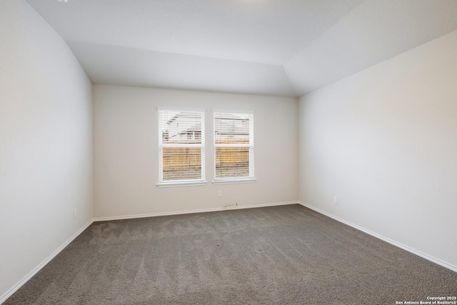 carpeted empty room featuring vaulted ceiling and baseboards