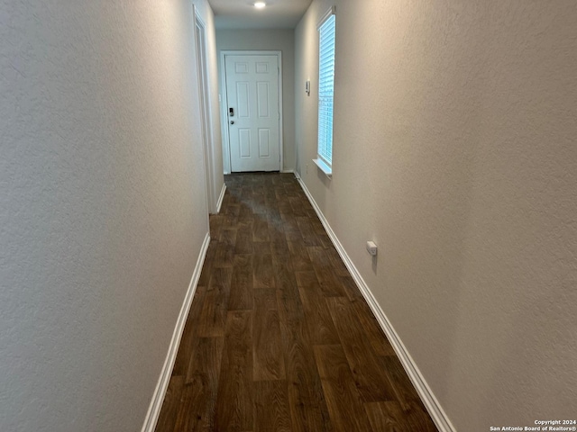 corridor featuring baseboards, dark wood-style flooring, and a textured wall