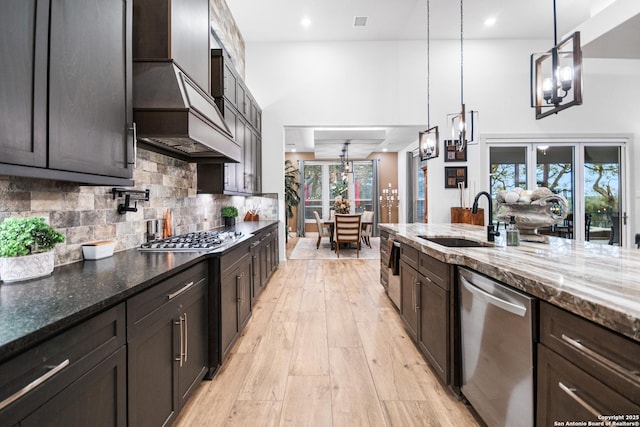 kitchen with light wood finished floors, decorative backsplash, dark stone countertops, stainless steel appliances, and a sink