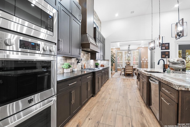 kitchen with light stone counters, a sink, appliances with stainless steel finishes, light wood-type flooring, and decorative backsplash