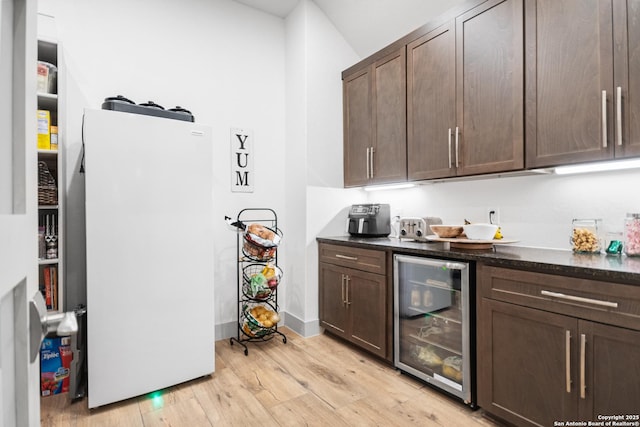 kitchen featuring beverage cooler, dark brown cabinets, light wood finished floors, and freestanding refrigerator