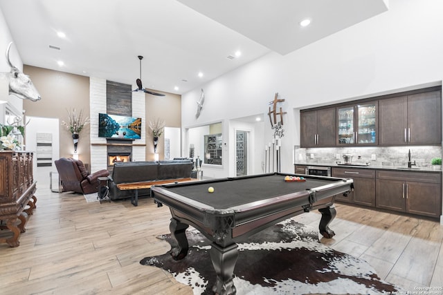 playroom featuring light wood-type flooring, a fireplace, a high ceiling, and wet bar