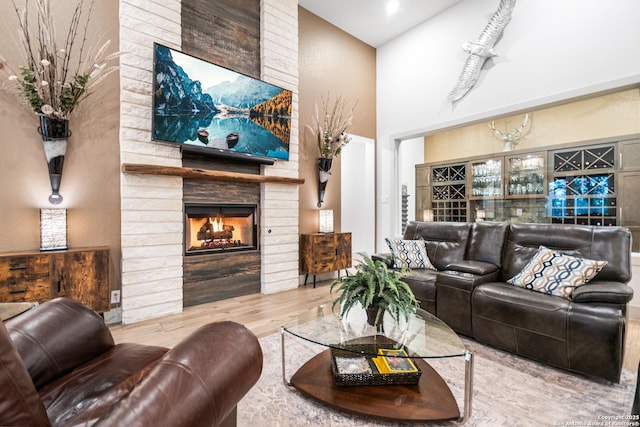 living area with a brick fireplace, wood finished floors, and a towering ceiling