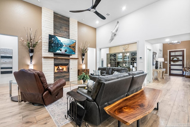 living area with a large fireplace, ceiling fan, light wood finished floors, and visible vents