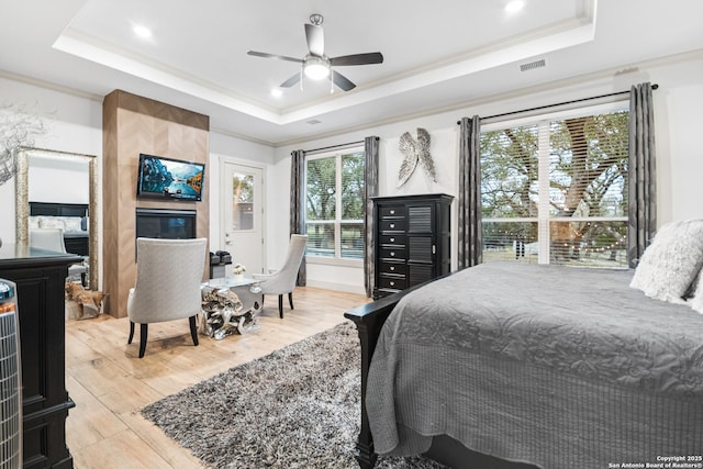 bedroom with ornamental molding, a tray ceiling, wood finished floors, and visible vents