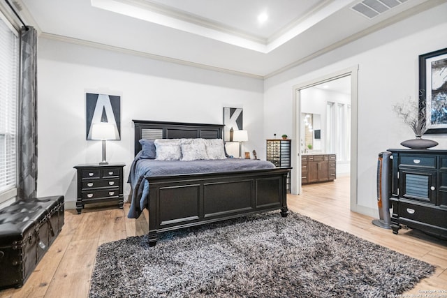 bedroom with light wood-style floors, visible vents, a tray ceiling, and crown molding