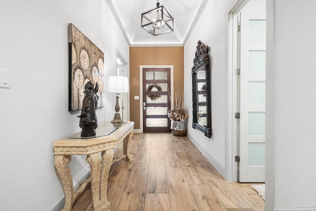 doorway to outside with light wood finished floors, baseboards, a chandelier, and ornamental molding