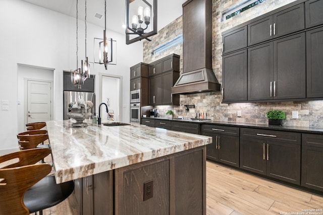 kitchen featuring tasteful backsplash, wall chimney exhaust hood, appliances with stainless steel finishes, a breakfast bar, and a sink