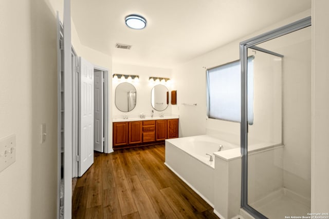 bathroom with double vanity, visible vents, wood finished floors, a garden tub, and a shower stall