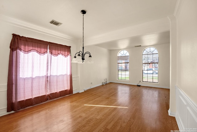 unfurnished dining area with baseboards, visible vents, wood finished floors, crown molding, and a chandelier