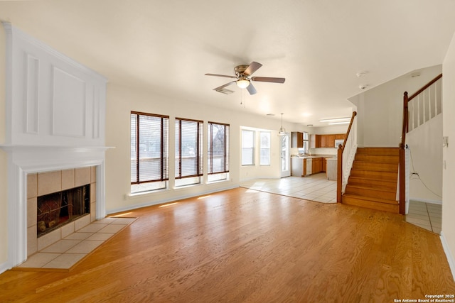 unfurnished living room with ceiling fan, light wood finished floors, stairway, and a tiled fireplace