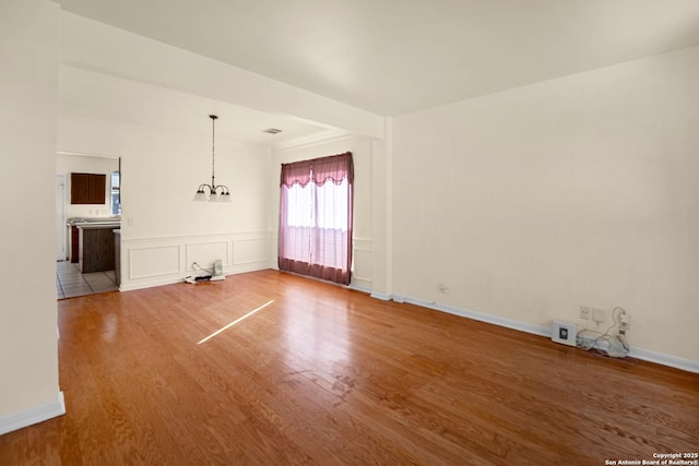 empty room featuring a notable chandelier, a decorative wall, baseboards, and wood finished floors