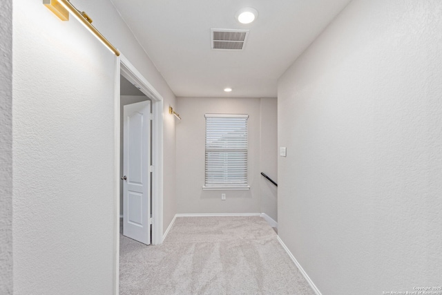 hall with an upstairs landing, baseboards, visible vents, and carpet flooring