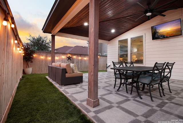 patio terrace at dusk with outdoor dining space, a fenced backyard, ceiling fan, and outdoor lounge area