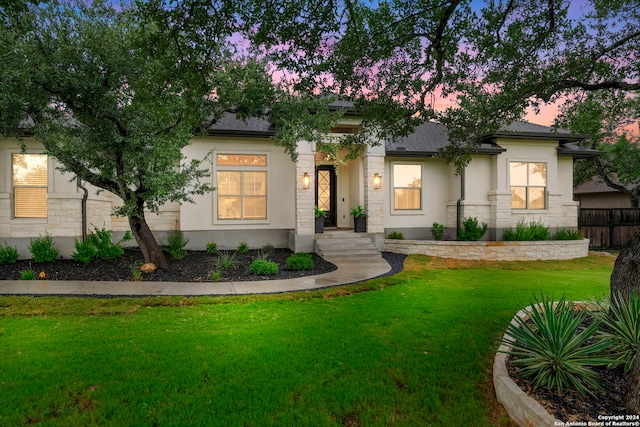 view of front facade with stucco siding, a front lawn, stone siding, fence, and roof with shingles