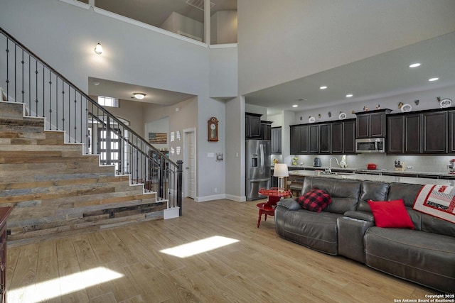 living area with stairway, a towering ceiling, light wood-style flooring, and recessed lighting