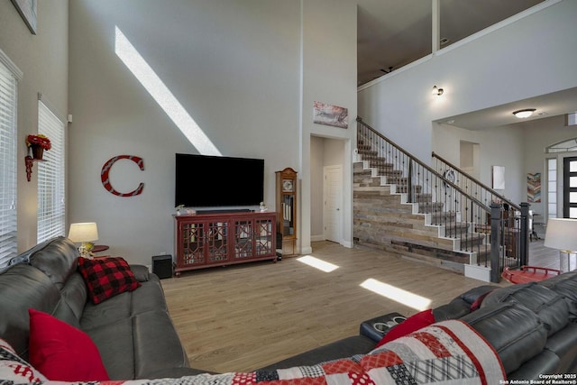 living room with a towering ceiling, stairs, and wood finished floors