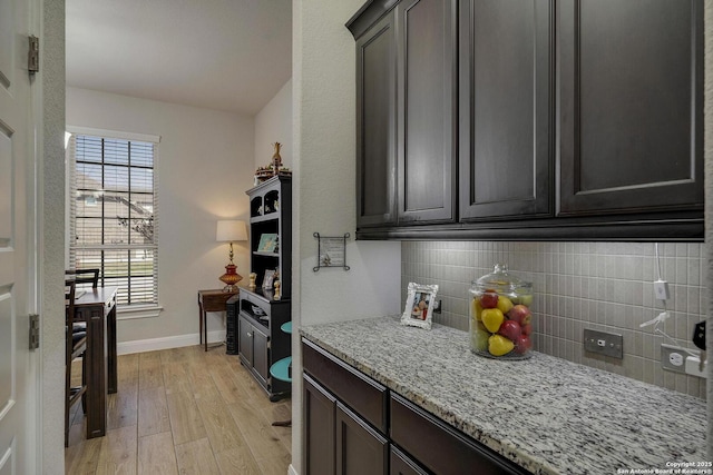 kitchen with baseboards, tasteful backsplash, light wood-type flooring, and light stone countertops