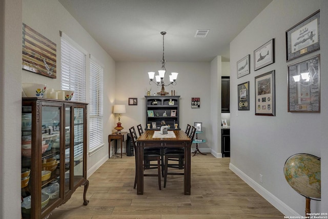 dining room featuring light wood-type flooring, baseboards, visible vents, and a chandelier