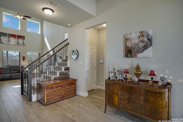 entryway with baseboards, visible vents, a towering ceiling, stairway, and wood finished floors