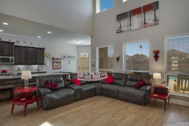 living area with recessed lighting, light wood-style flooring, and a towering ceiling